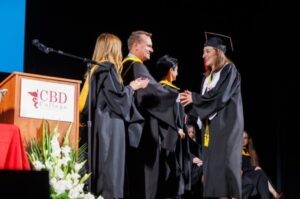 A female CBD College graduate receiving her certificate from a professor on stage during the graduation ceremony.