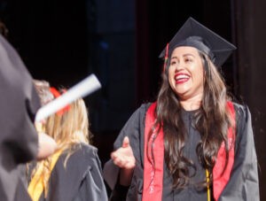 A smiling female graduate of CBD College receives her diploma.