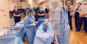 A group of doctors gathers inside the operating room, attentively listening to professors as they impart knowledge about surgical techniques and advanced technology. The atmosphere is focused and collaborative, as the doctors absorb valuable insights and expertise that will enhance their surgical practice and patient care. This exchange of knowledge underscores the importance of continuous learning and professional development in the medical field.