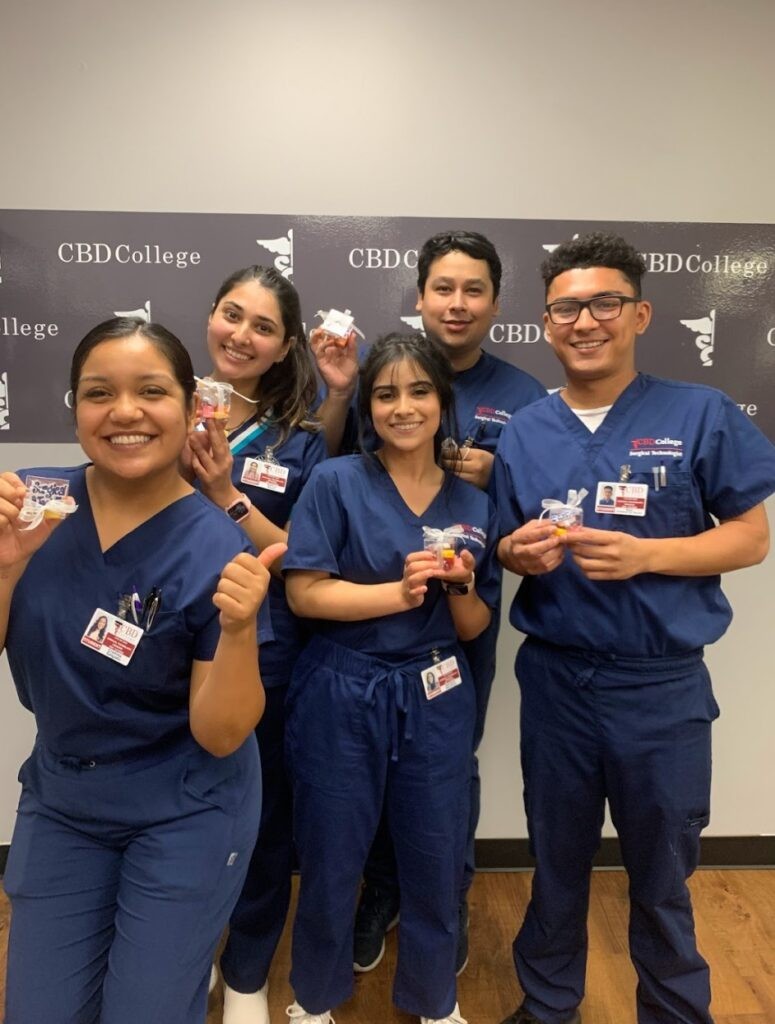 A group of trainee doctors from CBD College, clad in medical uniforms proudly displaying the college's logo, exude happiness and enthusiasm. Their smiles reflect the excitement and dedication to their medical education journey. This moment captures the camera and sense of achievement among the trainees as they prepare to embark on their careers in healthcare.