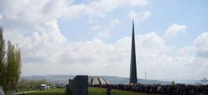 A solemn gathering at a memorial site on Armenian Genocide Memorial Day, with people paying respects and laying flowers in remembrance of the victims.
