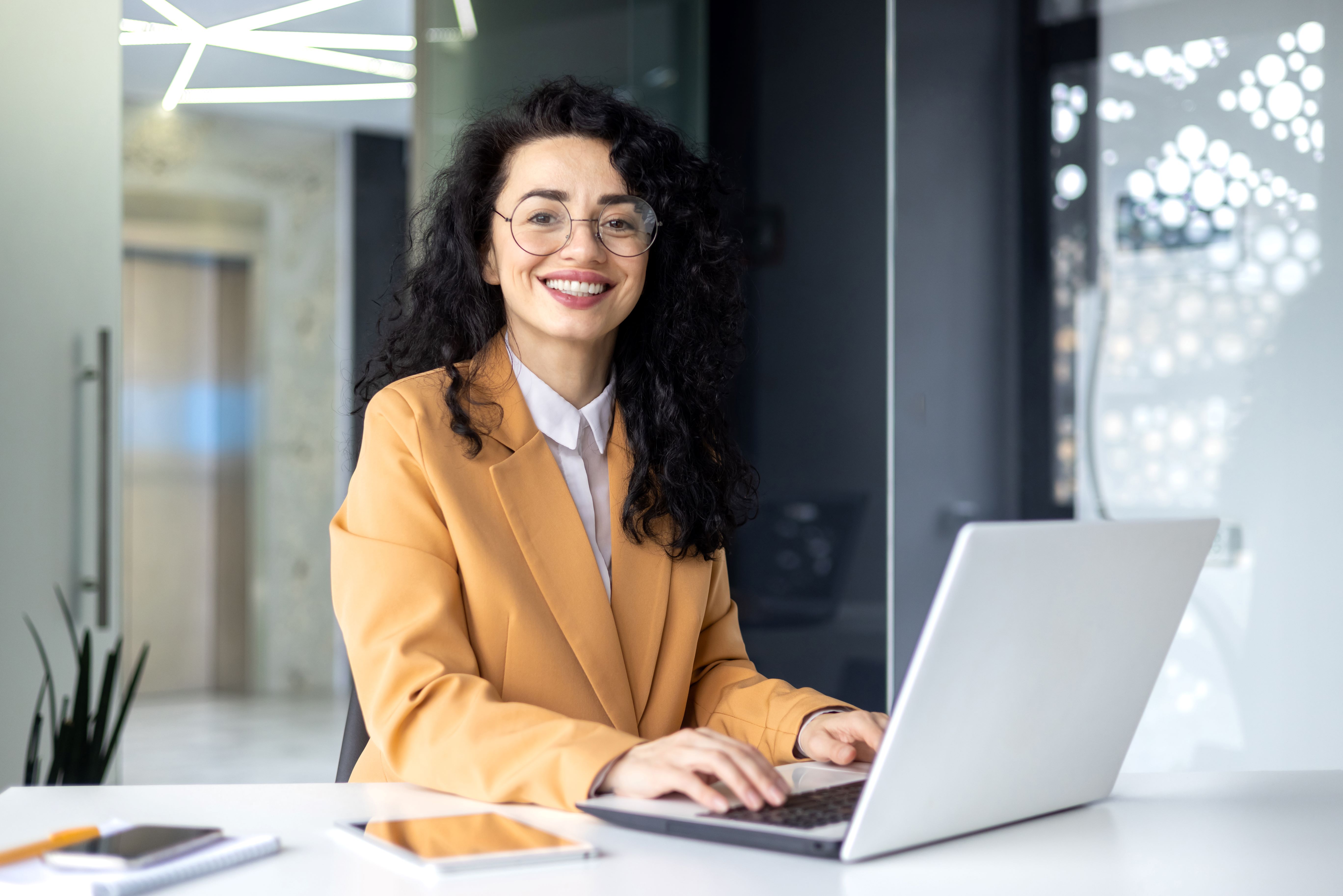 A woman specializing in health sciences sits at a desk, a computer before her, radiating a warm smile. Her demeanor reflects a positive and engaged presence as she likely navigates the intersection of technology and health sciences in her work or studies.