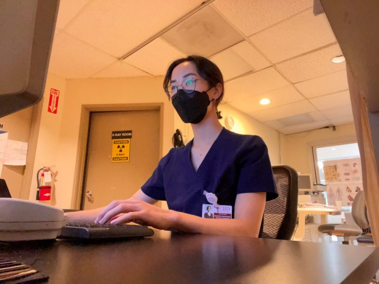 Liliane Tran, MRI Program student at CBD College, seated at a desk with a PC in a hospital setting.