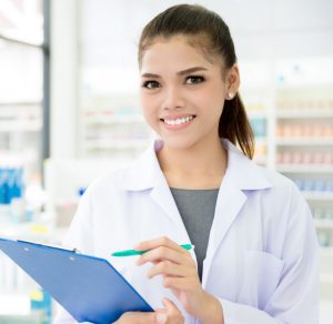 A smiling Asian female pharmacist working in a chemist shop or pharmacy.