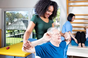 An elderly man receiving assistance from a nurse in a rehab clinic.