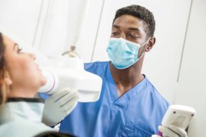 A young dentist, technician, or dental assistant using a modern digital X-ray device to capture an image of the jaw of a female patient, assessing the health of her teeth. The dental professional is carefully positioning the X-ray device on the patient's jaw.