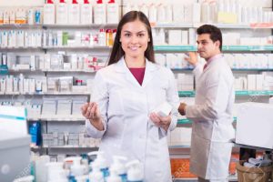 A female pharmacy technician counting pills behind the counter at a pharmacy.