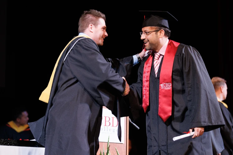 A proud CBD College graduate dons a distinctive graduation robe, expressing joy and pride as he warmly greets his professor. The special moment captures the sense of accomplishment and the bond between student and mentor